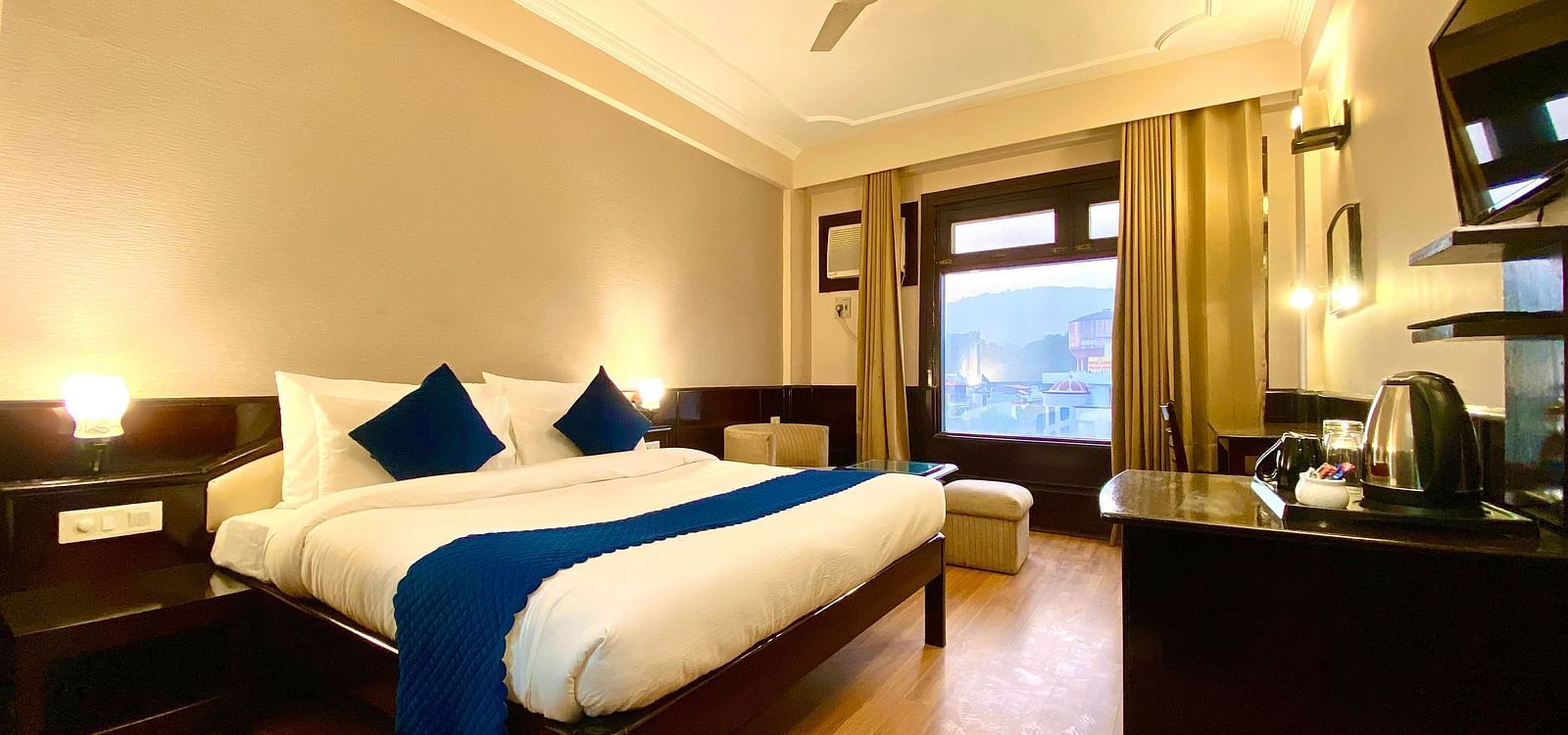 A hotel room with a king size bed, a desk, a chair, a flat-screen TV, and a window with a view of a lake  | DLS Park Grace, Haridwar